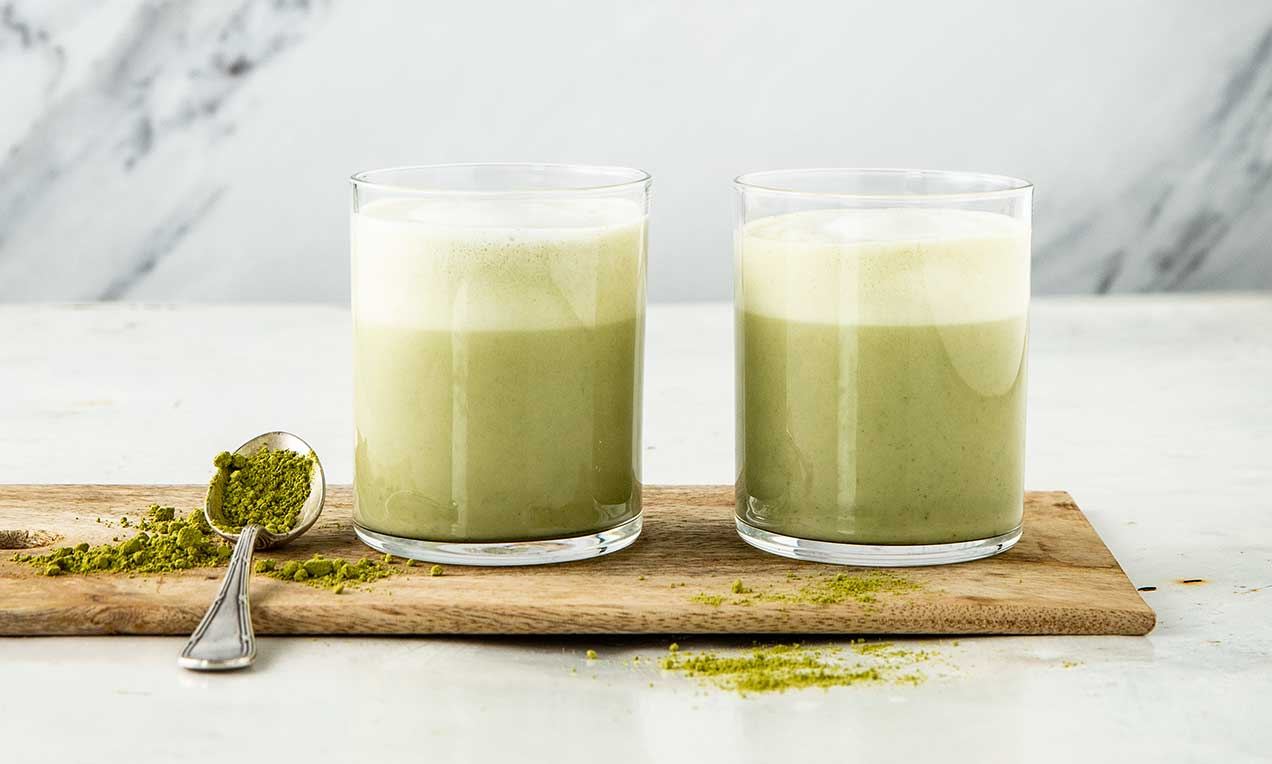 Ein Glas Matcha Latte mit Vanille steht auf einem Tisch, daneben ein Löffel.