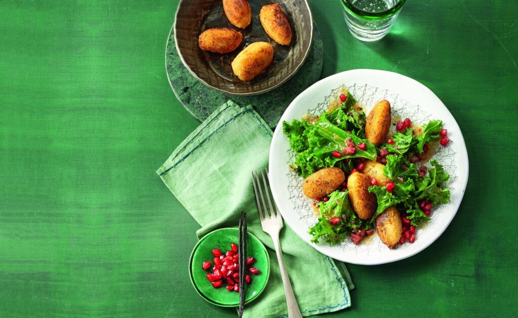 Grünkohlsalat mit gebratenen Kartoffelnocken auf einem weißen Teller angerichtet.
